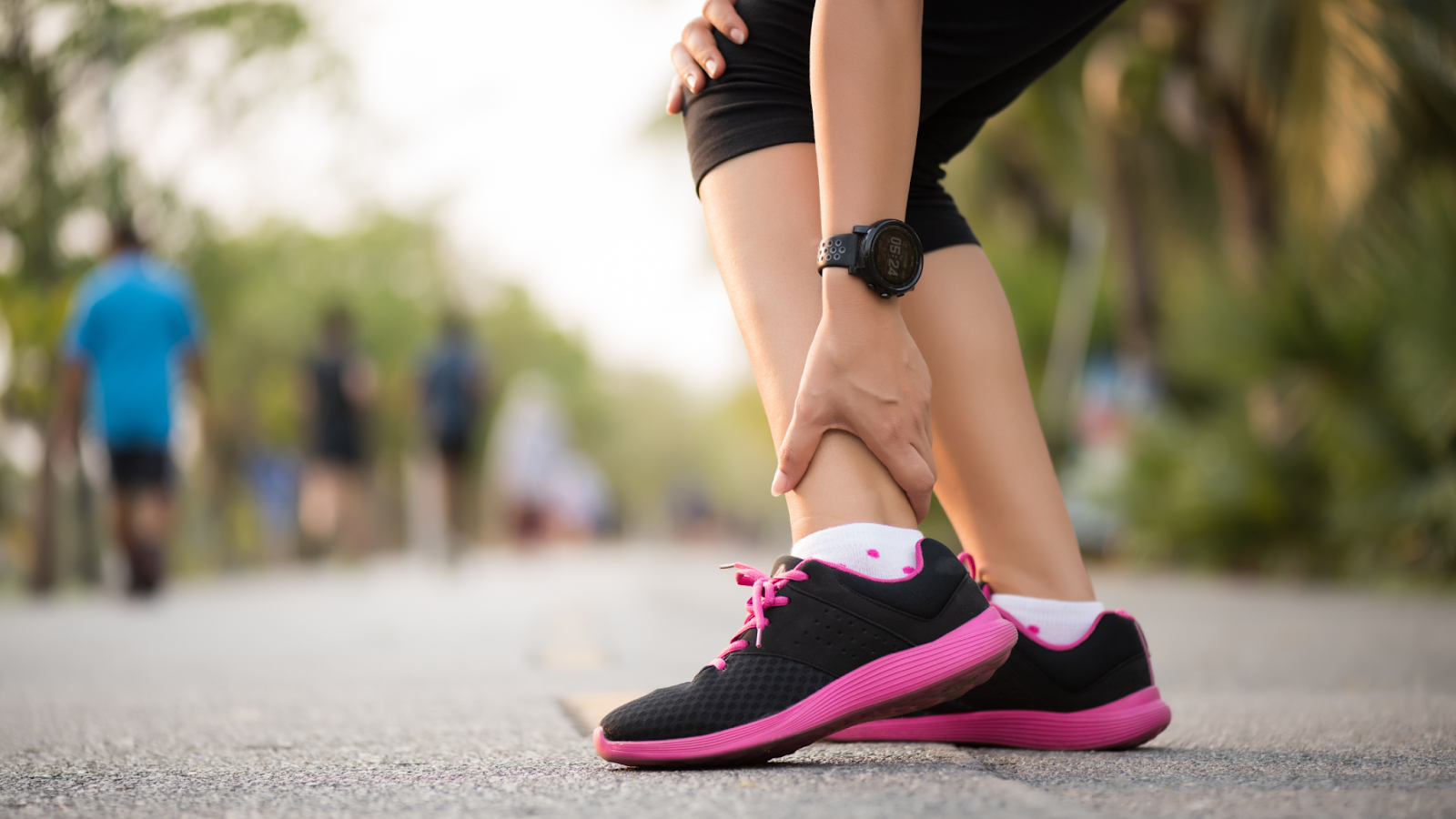 Woman left behind her running group as she bends over holding her injured ankle