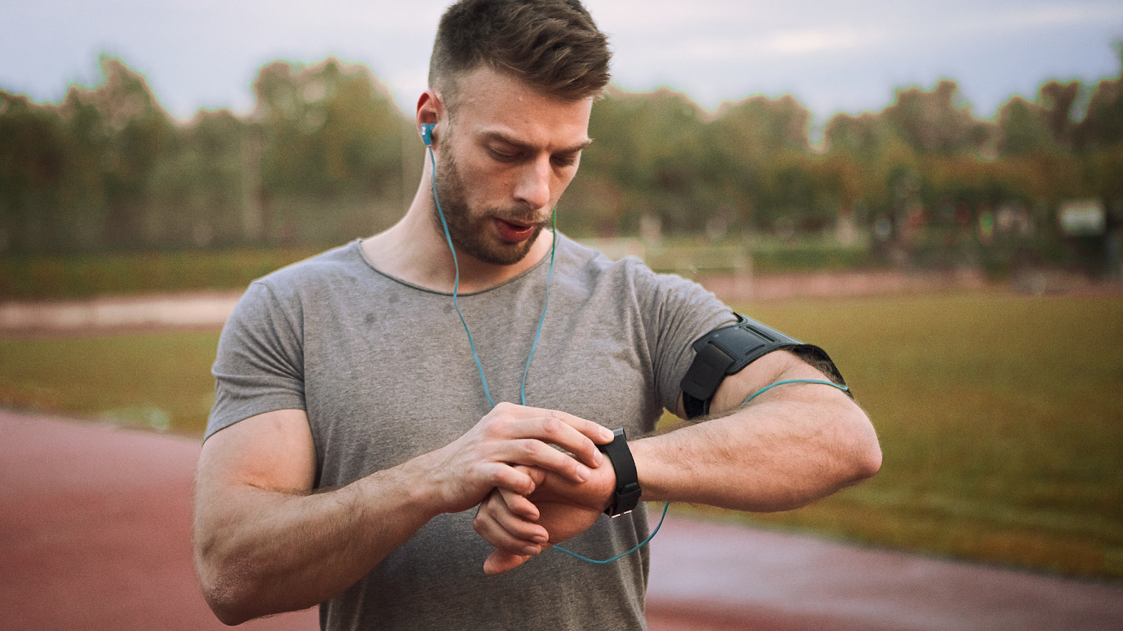 Man out on a run on the tracks pacing himself using a smart watch