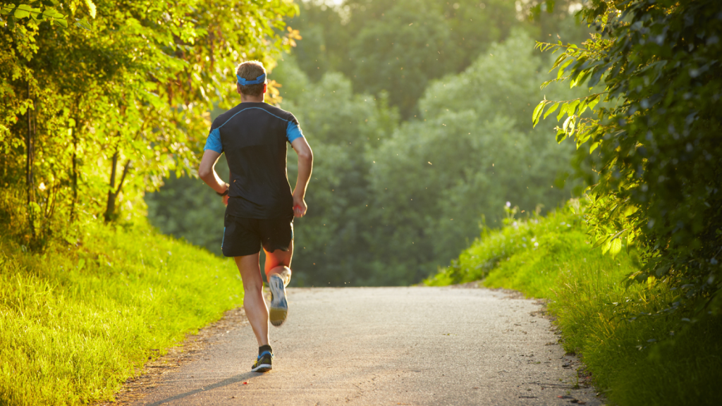 Man running on a paved path surrounded by lush green trees
