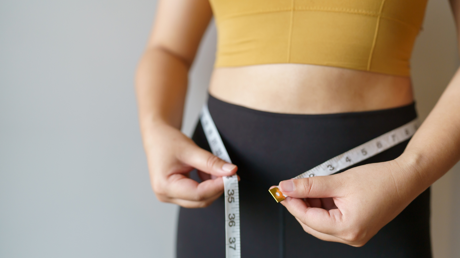 Woman in her running gear measuring her waist to see weight loss