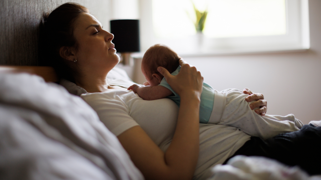 Tired woman lying in bed with her newborn baby